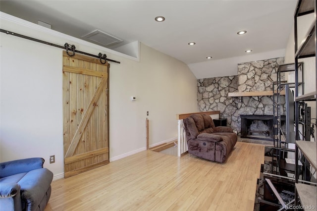 living room with hardwood / wood-style flooring, lofted ceiling, a barn door, and a stone fireplace