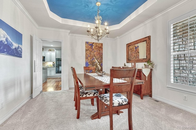 dining room with light carpet, a notable chandelier, ornamental molding, and a raised ceiling