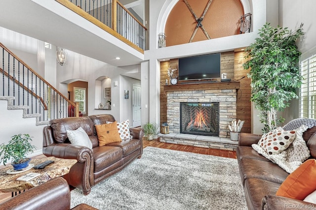 living room with hardwood / wood-style floors, a stone fireplace, and a towering ceiling