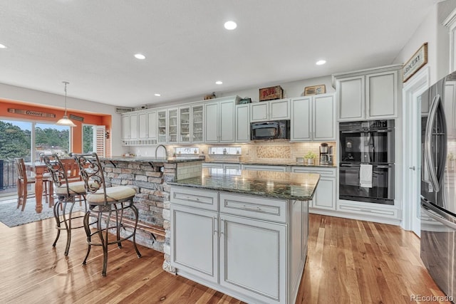 kitchen with a kitchen island with sink, dark stone countertops, black appliances, decorative backsplash, and decorative light fixtures