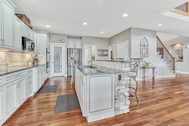 kitchen featuring an island with sink, sink, a kitchen bar, light stone counters, and black appliances