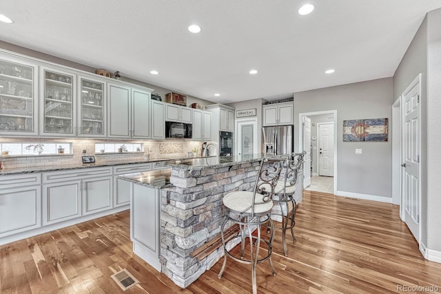 kitchen featuring stone counters, tasteful backsplash, a kitchen breakfast bar, a kitchen island with sink, and black appliances