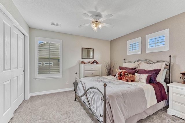 bedroom featuring light carpet, ceiling fan, a closet, and a textured ceiling