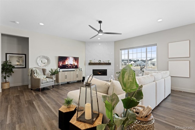 living room featuring ceiling fan, a large fireplace, and dark hardwood / wood-style flooring