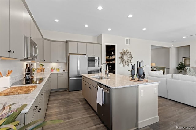 kitchen with sink, appliances with stainless steel finishes, an island with sink, gray cabinetry, and dark wood-type flooring