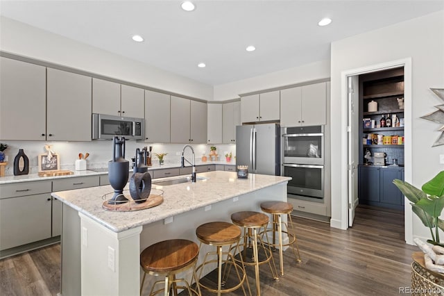 kitchen with gray cabinets, a center island with sink, sink, appliances with stainless steel finishes, and a kitchen breakfast bar