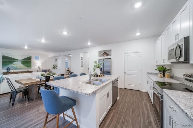 kitchen featuring sink, a kitchen breakfast bar, stainless steel appliances, white cabinets, and an island with sink