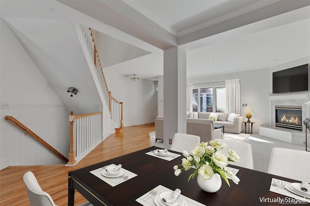 dining space with a high end fireplace, ornamental molding, stairs, and wood finished floors