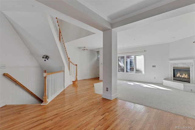 unfurnished living room with crown molding, light wood-style flooring, stairs, baseboards, and a tile fireplace