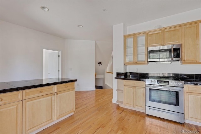 kitchen with light brown cabinetry, glass insert cabinets, light wood-type flooring, recessed lighting, and stainless steel appliances
