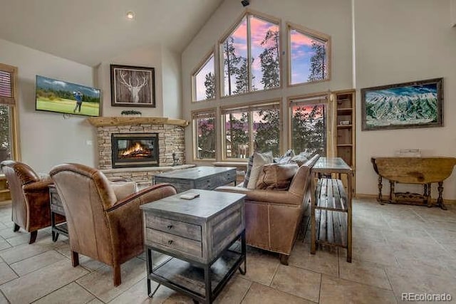 living area with high vaulted ceiling, a stone fireplace, and baseboards