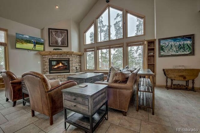 living room featuring high vaulted ceiling, a stone fireplace, and baseboards