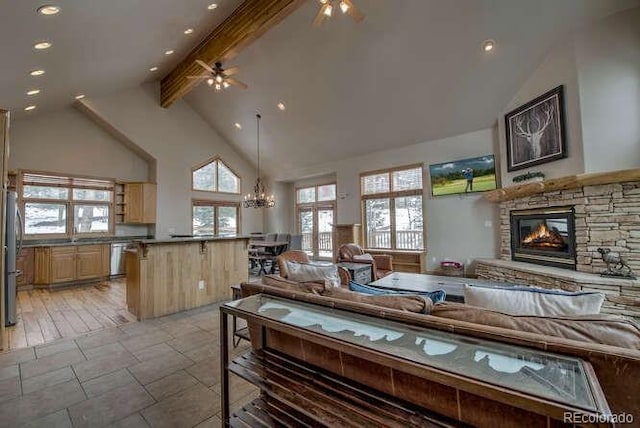 living area featuring beamed ceiling, a stone fireplace, high vaulted ceiling, a ceiling fan, and a chandelier