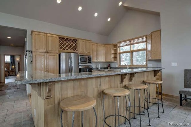 kitchen with stainless steel appliances, light brown cabinetry, high vaulted ceiling, light stone counters, and a breakfast bar area