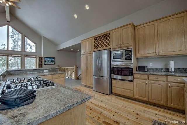 kitchen featuring stainless steel appliances, light brown cabinets, high vaulted ceiling, light stone countertops, and light wood-style flooring