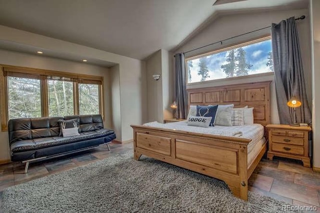 bedroom featuring multiple windows, stone tile flooring, lofted ceiling, and baseboards