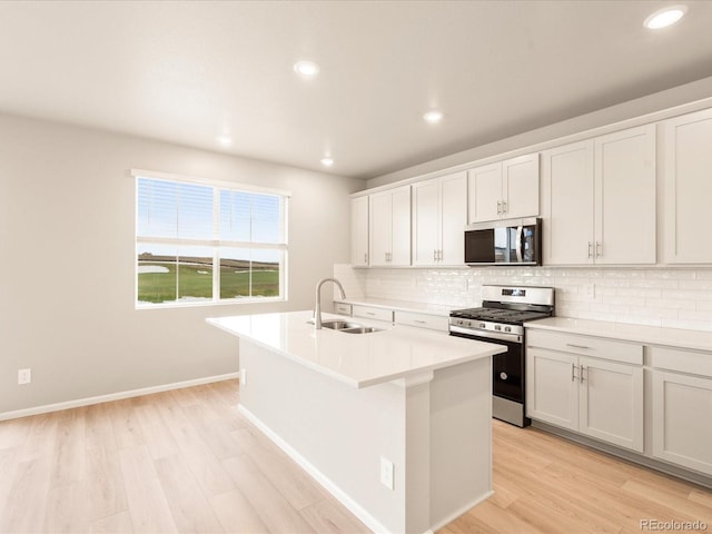 kitchen featuring light wood finished floors, an island with sink, a sink, decorative backsplash, and appliances with stainless steel finishes