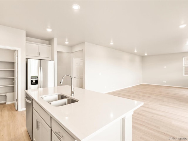 kitchen featuring light wood finished floors, a center island with sink, light countertops, appliances with stainless steel finishes, and a sink