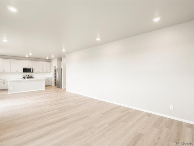 unfurnished living room featuring recessed lighting, light wood-style flooring, and baseboards