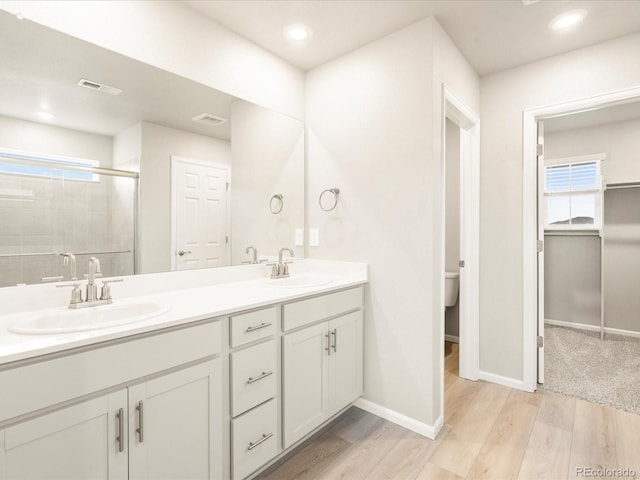 full bath featuring double vanity, a stall shower, wood finished floors, and a sink