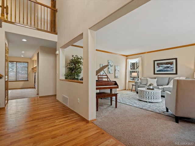 living room with crown molding, a towering ceiling, and light hardwood / wood-style flooring