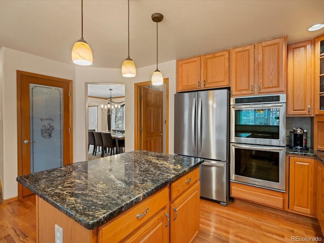 kitchen featuring light hardwood / wood-style flooring, appliances with stainless steel finishes, a center island, decorative light fixtures, and dark stone counters