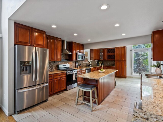 5884 S Hanover Way, Greenwood Village, CO 80111 - kitchen with appliances with stainless steel finishes, wall chimney range hood, decorative backsplash, a center island, and light stone counters