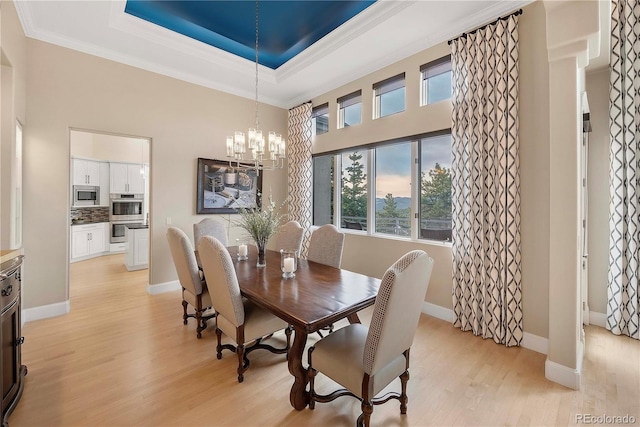dining area featuring a high ceiling, crown molding, light wood-type flooring, baseboards, and a chandelier