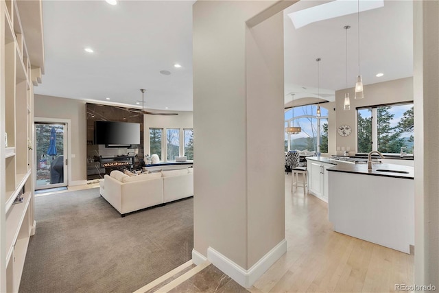 hall featuring baseboards, light wood-type flooring, recessed lighting, and a sink