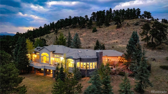 back of house at dusk with stone siding, a mountain view, and a tile roof