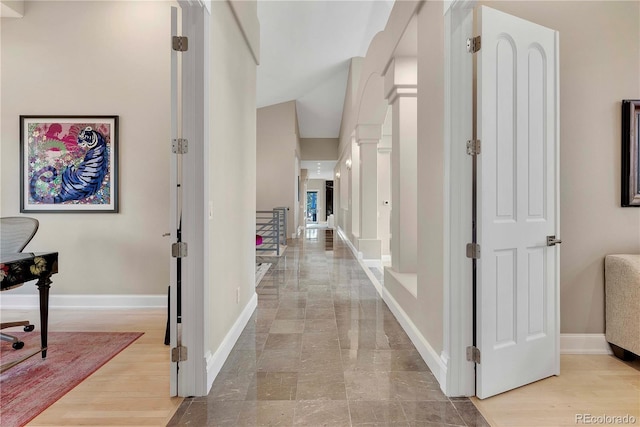 hallway featuring lofted ceiling and baseboards