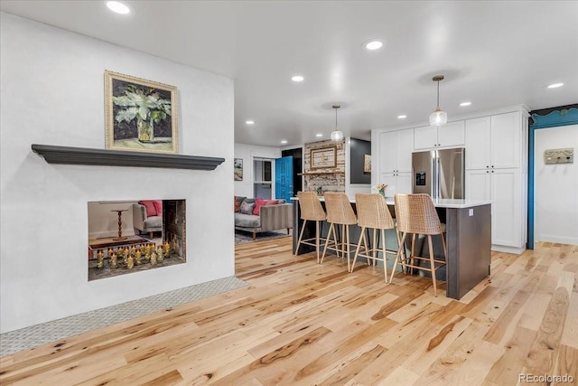 kitchen with decorative light fixtures, stainless steel fridge with ice dispenser, a multi sided fireplace, a kitchen breakfast bar, and white cabinets