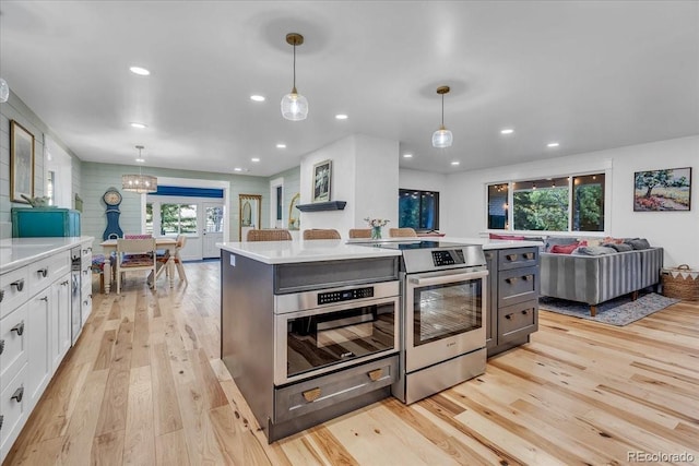 kitchen featuring appliances with stainless steel finishes, hanging light fixtures, a center island, white cabinets, and light wood-type flooring