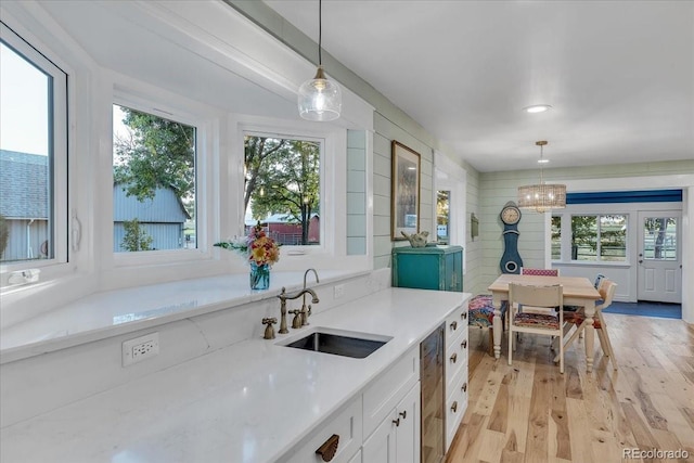 kitchen featuring pendant lighting, sink, white cabinetry, a notable chandelier, and light wood-type flooring