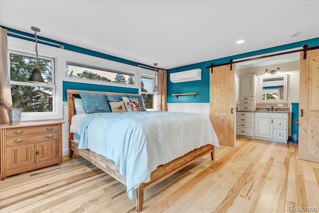 bedroom featuring sink, a wall mounted air conditioner, a barn door, and light hardwood / wood-style floors