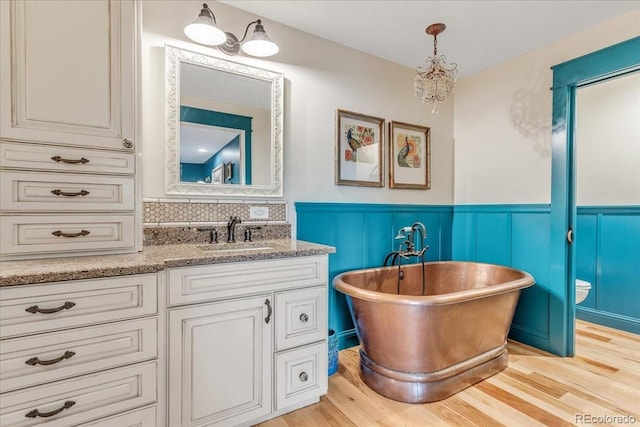 bathroom featuring a washtub, backsplash, vanity, wood-type flooring, and toilet