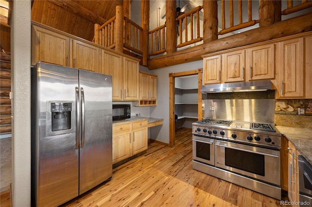 kitchen with high vaulted ceiling, under cabinet range hood, light wood-style flooring, baseboards, and appliances with stainless steel finishes