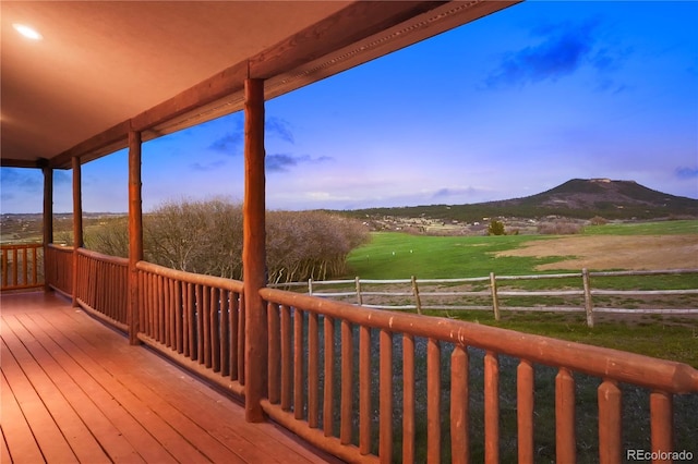 deck at dusk with a rural view, a mountain view, and fence