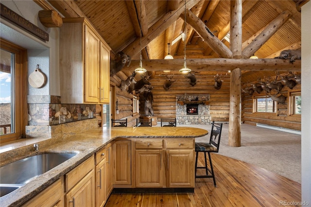 kitchen featuring rustic walls, a sink, a peninsula, beamed ceiling, and light wood-type flooring