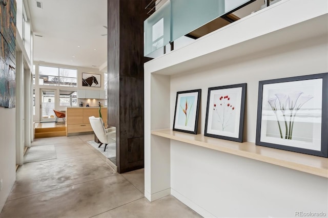 hallway with concrete flooring, a high ceiling, and baseboards