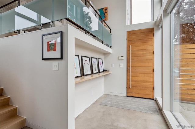 foyer with concrete flooring, baseboards, stairway, and a high ceiling