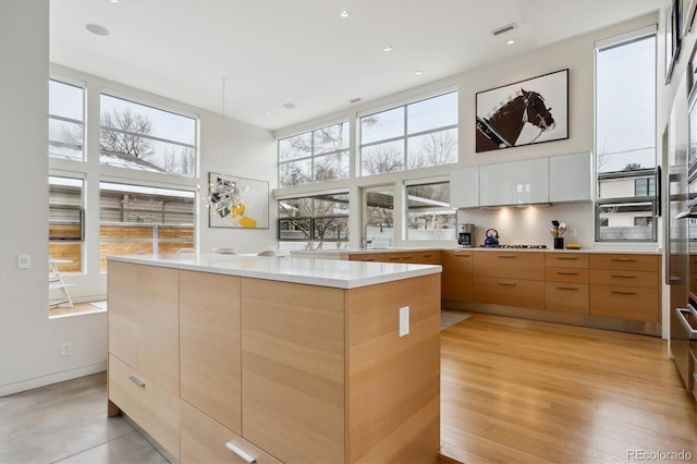 kitchen featuring white cabinets, a towering ceiling, modern cabinets, a center island, and light countertops