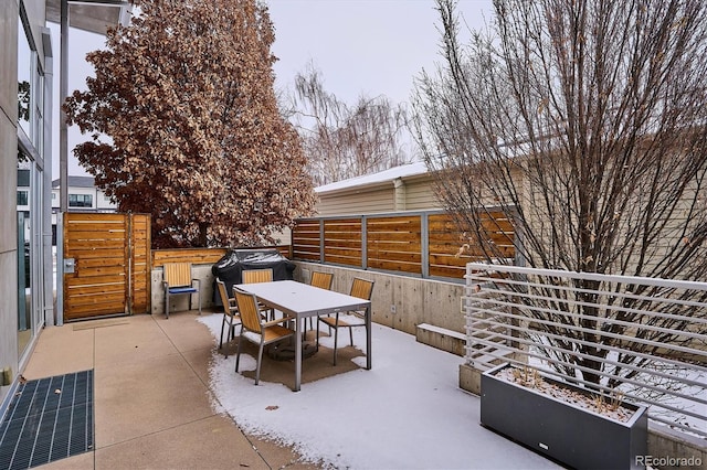 snow covered patio featuring outdoor dining area, fence, and a garden