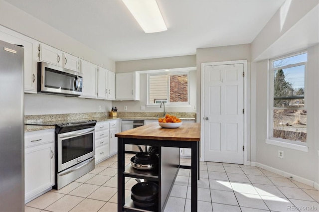 kitchen with light tile patterned floors, wood counters, appliances with stainless steel finishes, and white cabinets