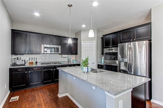 25046 E Bayaud Pl, Aurora, CO 80018 - kitchen with appliances with stainless steel finishes, dark wood finished floors, backsplash, an island with sink, and recessed lighting