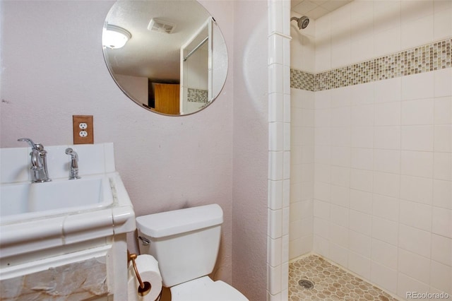 bathroom with tiled shower, sink, and toilet