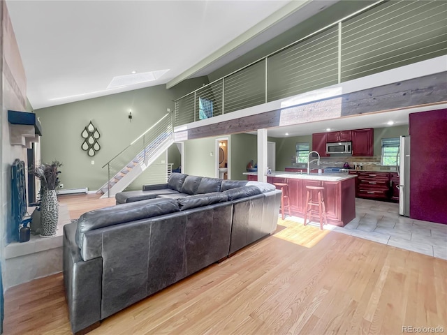 7085 Kiowa Rd, Larkspur, CO 80118 - living room with light wood-style flooring, stairs, a skylight, baseboard heating, and a high ceiling