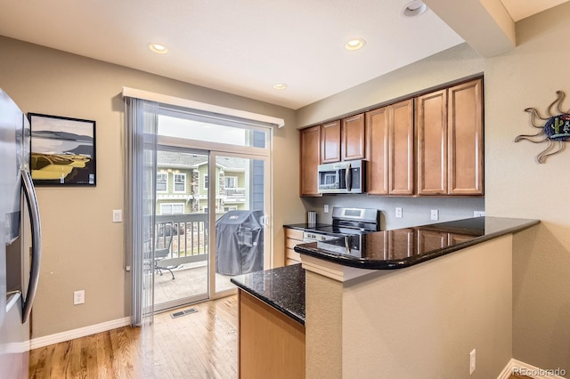 9381 Ashbury Cir Unit 105, Parker, CO 80134 - kitchen with appliances with stainless steel finishes, brown cabinets, dark stone counters, light wood finished floors, and a peninsula
