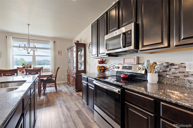 2200 Cadman St, Berthoud, CO 80513 - kitchen with appliances with stainless steel finishes, light wood-style floors, a chandelier, dark stone counters, and pendant lighting