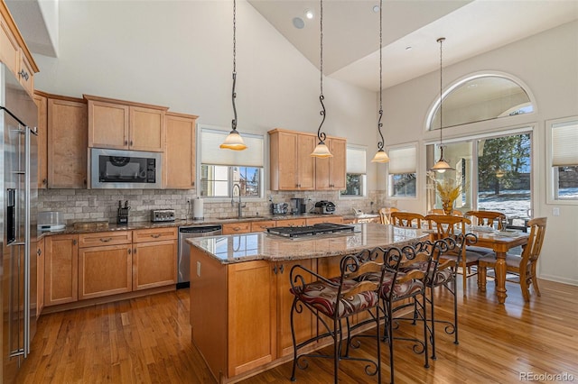 kitchen featuring high vaulted ceiling, hanging light fixtures, a kitchen island, light stone counters, and stainless steel appliances